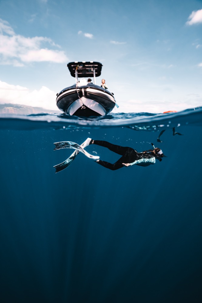 Split frame: expedition boat above, freediver below, Tahiti